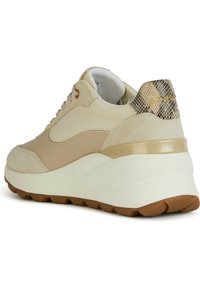 Sneaker beige con tomaia in suede e materiale sintetico, dotata di un tacco con accentuazione dorata texturizzata e di una suola bianca spessa con una suola esterna marrone texturizzata.