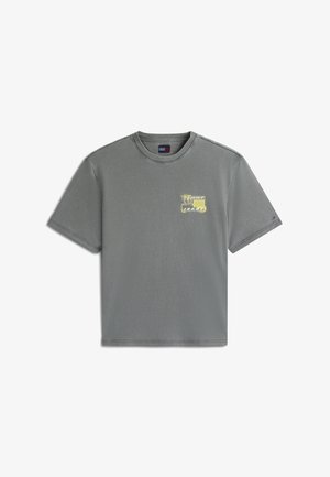 Camiseta gris de manga corta con cuello redondo, con un pequeño gráfico amarillo y negro en el lado izquierdo del pecho y un pequeño detalle de bandera en la manga izquierda.