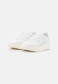 Bílé tenisky s hladkým koženým svrškem, kulatou špičkou a texturovanými detaily na patě. Mají kontrastní švy a silnou podrážku.