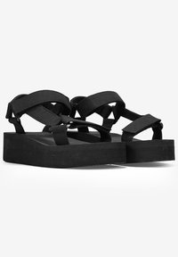 Le sandali platform nere presentano suole spesse e texturizzate e cinturini incrociati realizzati in un morbido tessuto, progettati per comfort e facilità d'uso.