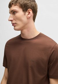 T-shirt corto marrone a maniche corte realizzato in tessuto morbido, con scollatura a girocollo e un sottile logo "BOSS" impresso sul petto.