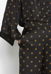 Black satin outfit featuring a loose fit, wide sleeves, and a belt. Decorated with gold circular patterns. Buttons on the front add detail.