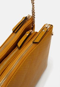 Borsa gialla in tessuto testurizzato con un esterno a fantasia, due scomparti con zip e una tracolla in catena metallica. Rifinita con hardware in tonalità oro.
