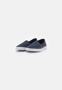 Los zapatos slip-on de lona azul marino cuentan con una suela de goma blanca, punta redonda y lados elásticos para facilitar su uso. Diseño simple y versátil.