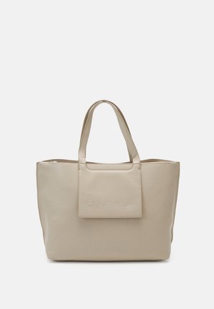 Beige leather Calvin Klein tote bag with double handles and a front flap pocket, minimalist design on a plain background.