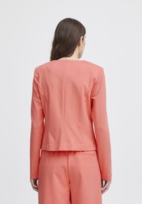 Koraalkleurige lange mouwen jacket met een rechte snit en een detail in de achterkant, gecombineerd met bijpassende broeken met een achterzak. Soepele textuur.