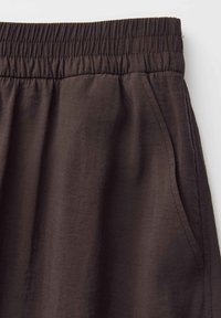 Pantalon marron foncé avec taille élastique et poches latérales, montrant la texture du tissu et les détails des coutures.