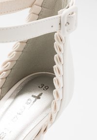 Bílá sandála na podpatku s výrazným zakřiveným designem, zdobená texturovanými detaily a kovovou vnitřní stélkou. Velikost 39 je viditelná na podrážce.