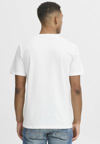 Tricou alb din bumbac, cu guler rotund și mâneci scurte, având o textură netedă. Partea din spate prezintă un design simplu, nedecorat.