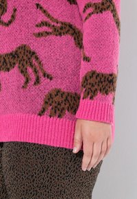 Maglione lavorato a maglia rosa con motivo leopardato marrone, con polsini e orlo a costine. Inquadratura ravvicinata che mette in evidenza il dettaglio della manica e della trama.