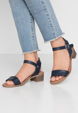 Navy blue leather sandals with a mid-height block heel, wide strap over the toes, and an adjustable ankle strap with a buckle.