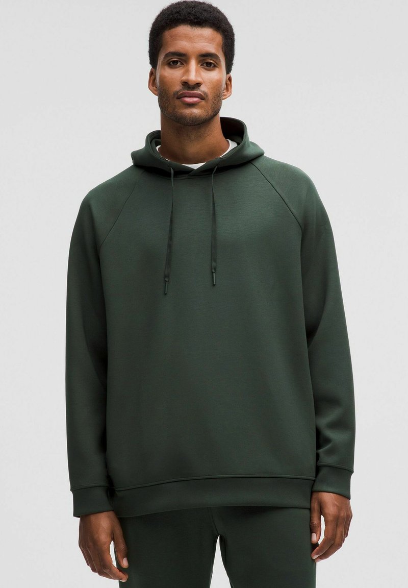 Tumma vihreä huppari, joka on valmistettu pehmeästä kankaasta. Siinä on etupuolella kengurutasku, säädettävä nyöri huppu sekä ribbikangasta hihansuissa ja helmassa.