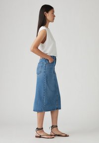 Μπλε τζιν μίντι φούστα σε ανοιχτό μπλε χρώμα, με ίσια γραμμή, ξεφτισμένο τελείωμα και δύο πίσω τσέπες. Συνδυάζεται με λευκό αμάνικο τοπ και μαύρα σανδάλια.