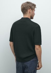 Svart kortärmad polo skjorta med en texturerad ribbad design, med en spridd krage och horisontella ribbade detaljer på axlarna.