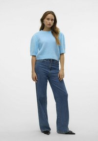 Gaiši zils adīts džemperis ar īsām puff piedurknēm, apvienots ar augsta jostasvietas zila džinsa biksēm un norādītām melnām kurpēm.