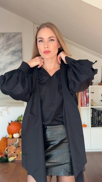 Top nero con maniche a sbuffo, scollatura a V e apertura frontale, abbinato a una gonna nera in pelle con impresso motivo coccodrillo. Texture lisce e vestibilità affusolata.