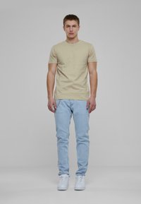 Camiseta de manga corta beige combinada con jeans ajustados de color azul claro y zapatillas blancas. El conjunto tiene una estética casual y cotidiana.