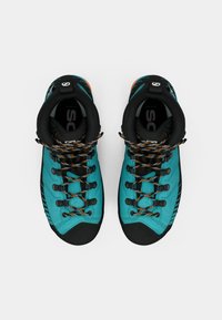 Um par de botas de caminhada em azul-turquesa e preto com atacadores em laranja visto de cima sobre um fundo branco.