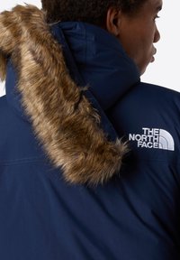 Parka blu navy con bordo in pelliccia sintetica e logo ricamato. Presenta un materiale resistente e un design strutturato per garantire calore.