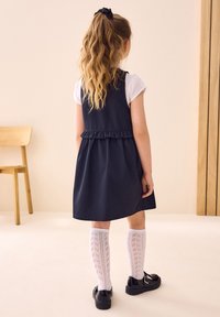 Meresinine kleit volangidega vöökohas, kantud valgete p�õlvikutega, millel on mustriline disain, ning mustade kingadega.