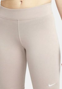 Ljusbeige leggings med slät textur, hög midja och sömdetaljer. Har en liten vit Nike-logotyp på nedre vänstra benet.