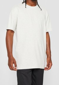 Světle šedé tričko s krátkým rukávem v uvolněném střihu, vyrobené z měkké látky s hladkým povrchem. Obsahuje kulatý výstřih a minimalistický design.