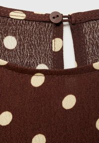 Brown polka dot fabric with cream-colored spots, showing a button closure at the back and a textured weave pattern.