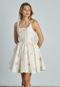 Vestido de lino con estampado floral en crema, con un corpiño ajustado, escote cuadrado y falda acampanada. Acentos en rosa claro y verde por toda la prenda.