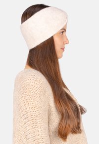 Bandeau en tricot beige clair fabriqué à partir de matériau doux, avec un design torsadé et une large bande couvrant les oreilles, associé à un pull confortable.