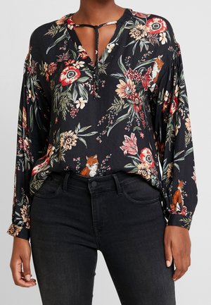 Blouse noire à manches longues avec un motif floral rouge et crème et de petites illustrations de renards, associée à un jean noir taille haute.