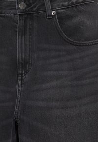 Close-up of black denim jeans showing button, belt loop, front pocket, and metal rivets.