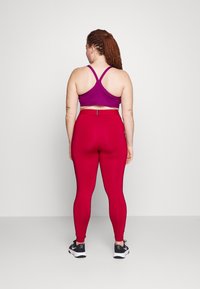 Tenue de sport ajustée composée d'un soutien-gorge de sport violet à dos nageur et de leggings rouges, tous deux en matière extensible. Baskets noires avec accents blancs.