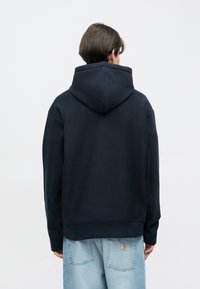 Μπλε ναυτικό φούτερ με μεγάλο κουκούλι, κατασκευασμένο από απαλό υλικό. Διαθέτει μακριά μανίκια και άνετη εφαρμογή, συνδυασμένο με τζιν ανοιχτού χρώματος.