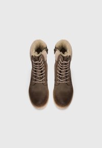 Bottines en cuir marron avec un col beige duveteux, un laçage à l'avant et une fermeture éclair sur le côté. Surface texturée et semelle de couleur claire.