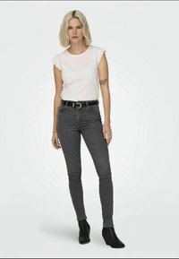 Top alb cu mâneci scurte și dantelă la margine, asociat cu blugi skinny gri închis și cizme cu toc negre. Design simplu și siluetă ajustată.