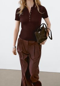 Burgundyribbad polo shirt med korta ärmar och knappslå, tillsammans med högmidjade, löst sittande bruna byxor och en liten mörk handväska.