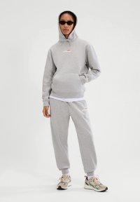 Set di felpa grigia e pantaloni tuta in cotone misto, con tasca anteriore, cappuccio con cordino e logo. Abbinato a scarpe da ginnastica.