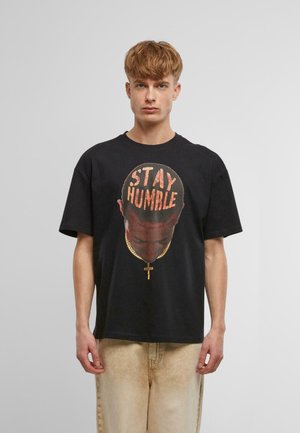 Svart bomull T-skjorte med et stort grafisk motiv av et hode med teksten "STAY HUMBLE", detaljert tekstur og en gullkjede med et kors som aksent.