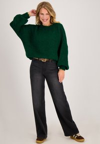 Groen gebreide trui met een losse pasvorm en verzonken schouders, gecombineerd met hooggetailleerde zwarte jeans en bruine schoenen met witte accenten.