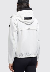 Veste blanche avec une capuche, un ourlet élastique et des accents noirs. Présente un logo au dos en noir. Matériau lisse et léger.