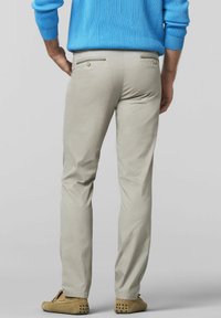 Hellbeige Baumwollhose im schmalen Schnitt, mit zwei Gesäßtaschen und Knopfverschlüssen sowie dezenten Nähdetails. Kombiniert mit einem blauen Pullover.