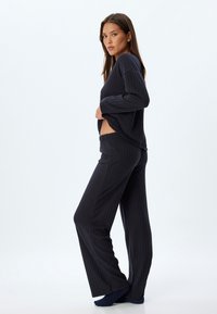 Donkere geribbelde lounge set met een losvallende longsleeve top en wijde broek. De stof heeft een zachte textuur en een subtiele glans.