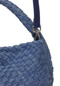 Blå vævet håndtaske med et struktureret denim-lignende materiale, en glat blå læderrem og sølvhardware til fastgørelse.