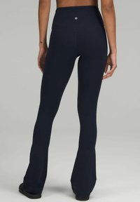 Granatowe legginsy dzwonowe z wysokim stanem, wykonane z gładkiego materiału z logo z tyłu, zaprojektowane z myślą o komforcie i swobodzie ruchów.