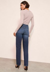 Top de manga larga de canalé color beige claro y jeans rectos de talle alto en azul oscuro con dobles bolsillos traseros y detalles de costura sutiles.