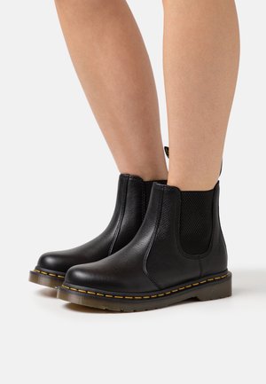 Botines de cuero negro hasta el tobillo con paneles laterales elásticos, costuras amarillas y suelas de goma. Acabado texturizado y lengüeta en la parte trasera.