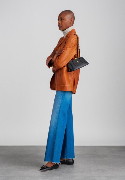 Blazer de pele castanha, suéter de gola alta bege, jeans azul de perna larga com bainha desfiada, mala preta e sapatilhas pretas.