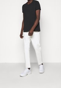 Czarna bawełniana koszulka z podwiniętymi rękawami, w połączeniu z białymi spodniami o prostym kroju i białymi trampkami. Prosty, minimalistyczny design z luźnym krojem.