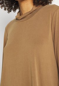 Brun långärmad topp med en krage av modell cowl, tillverkad av ett mjukt och slätt tyg. Har en minimalistisk, sömlös konstruktion.