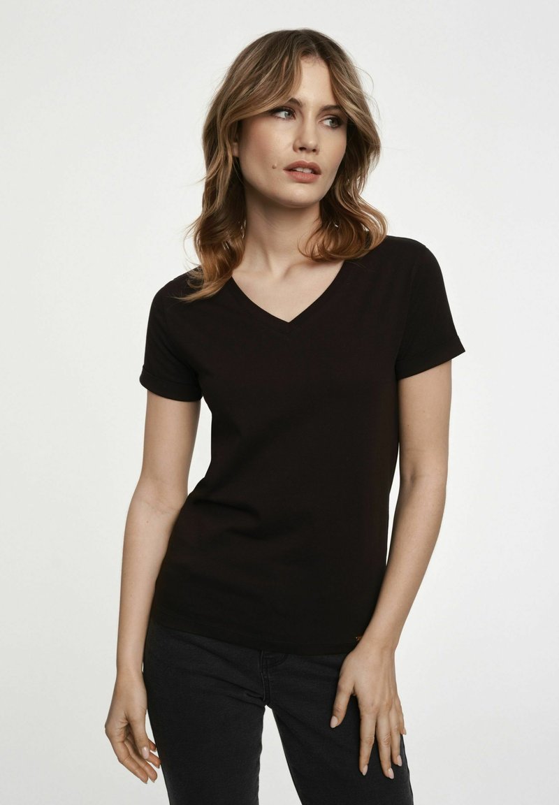 Czarna koszulka V-neck z krótkim rękawem, wykonana z miękkiego materiału, dopasowany krój, gładka faktura z minimalnymi detalami, w połączeniu z ciemnymi dżinsami.